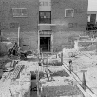 Construction workers are busy in an excavated area, laying foundations for a building with LMB logo watermark overlay.