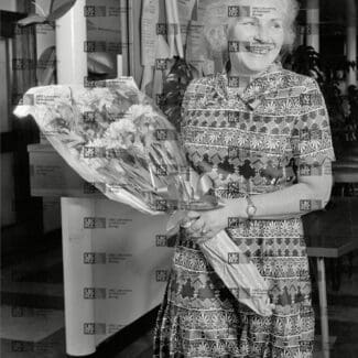 Gisela Perutz holding bouquet of flowers with LMB logo watermark overlay.