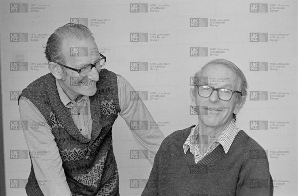 César Milstein and Fred Sanger with LMB logo watermark overlay.