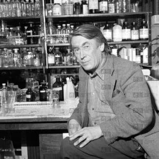 John Smith sitting in front of shelving holding several glass bottles with LMB logo watermark overlay.