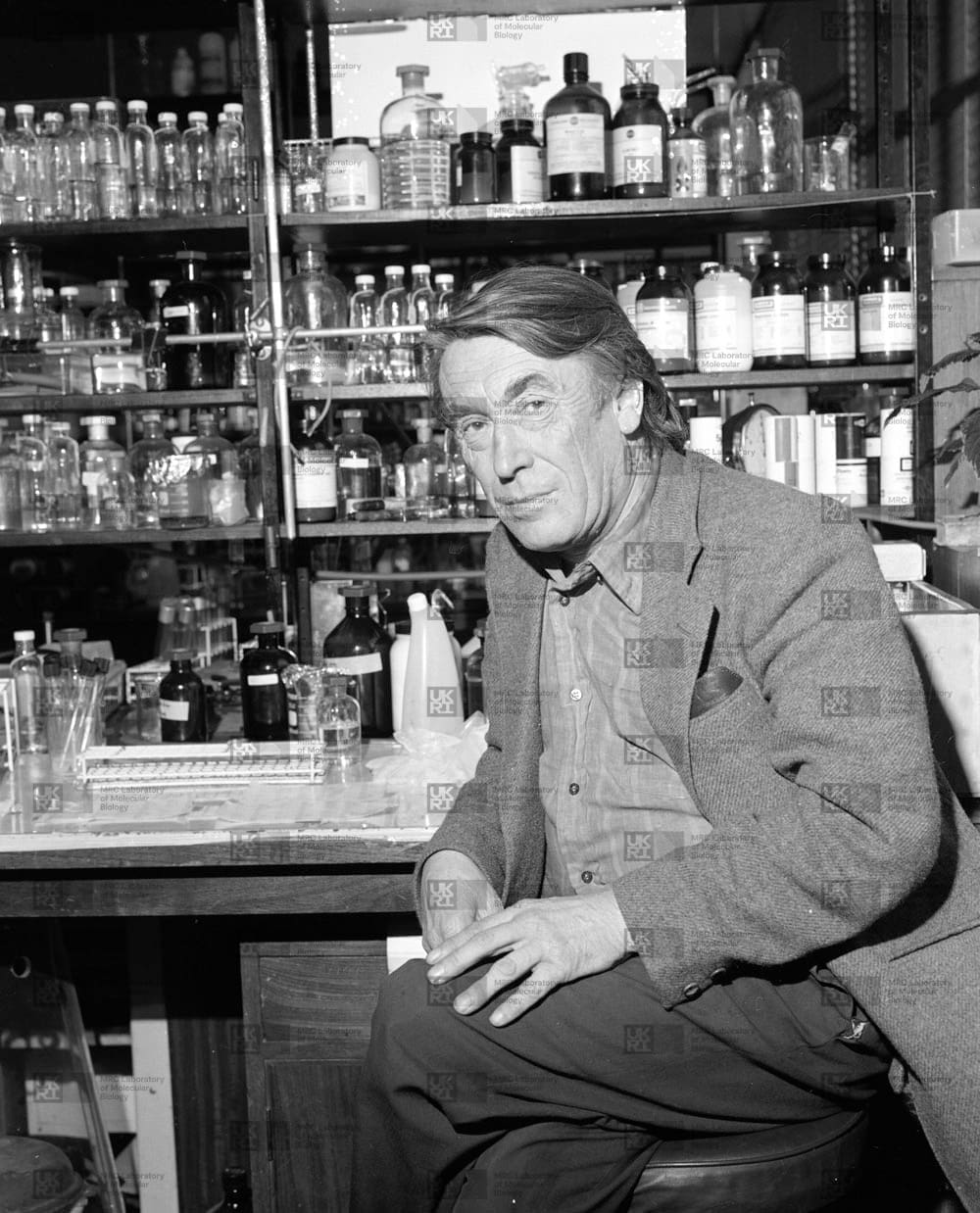 John Smith sitting in front of shelving holding several glass bottles with LMB logo watermark overlay.