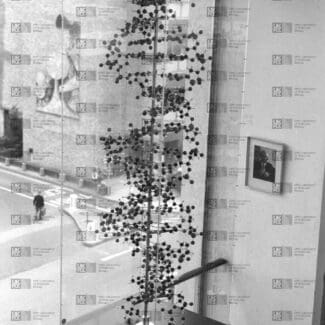 Tall ball-and-spoke model of a double helix in a transparent case, displayed indoors with a street scene visible outside with LMB logo watermark overlay.