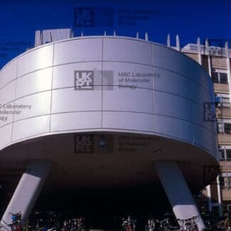 A circular, elevated MRC Laboratory of Molecular Biology building surrounded by other modern laboratory structures under a clear blue sky with LMB logo watermark overlay.