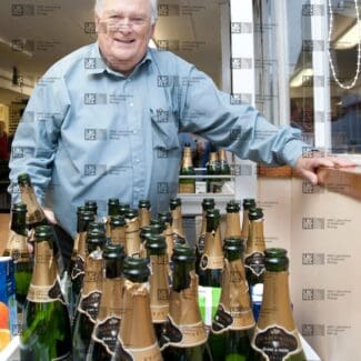 Michael Fuller stood behind several empty champagne bottles, with LMB logo watermark overlay.