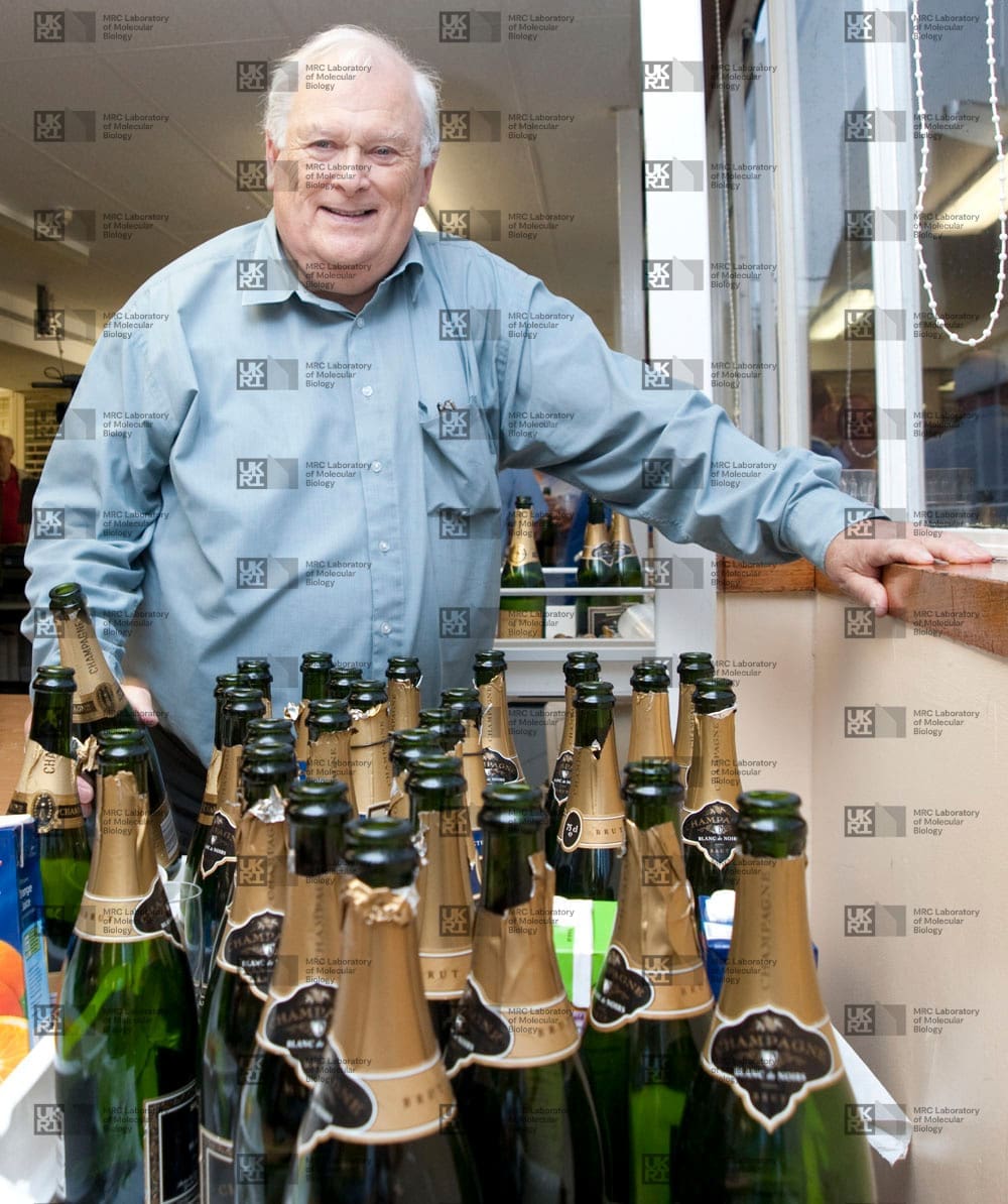 Michael Fuller stood behind several empty champagne bottles, with LMB logo watermark overlay.