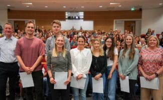 Group of people holding certificates, stood in front on packed lecture theatre