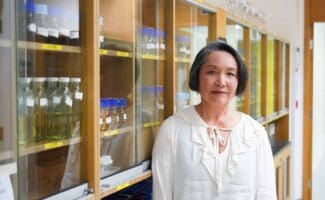 Kaz Collins, stood in front of cupboards holding glass bottles