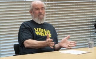 Martin, sat at a wooden desk, speaking whilst gesturing with his hands in front of him.