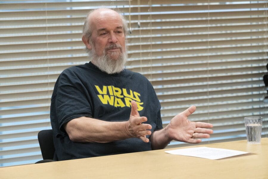 Martin, sat at a wooden desk, speaking whilst gesturing with his hands in front of him.