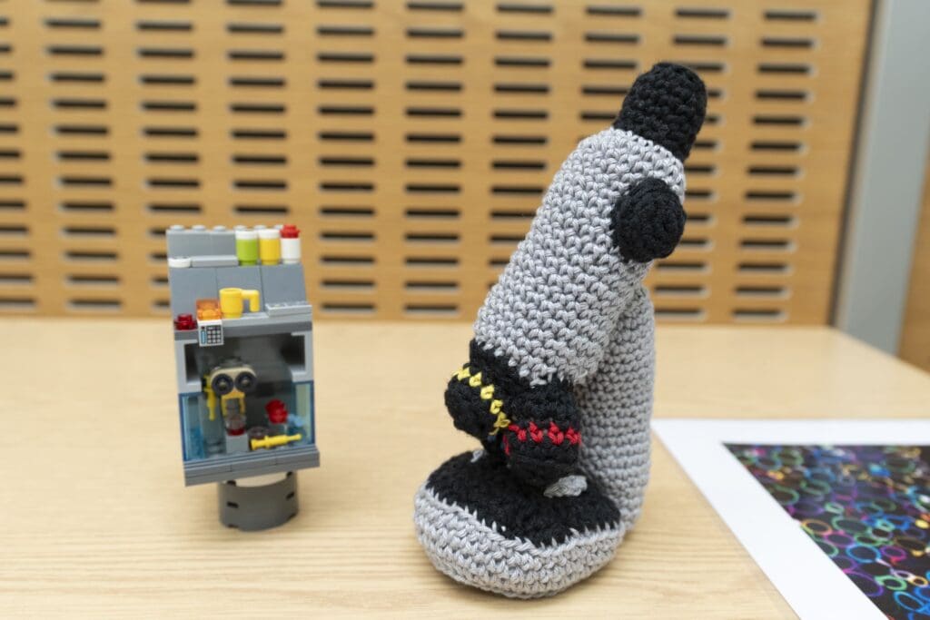 Lego structure of scientific equipment and crocheted microscope, with a colourful scientific image partially visible.