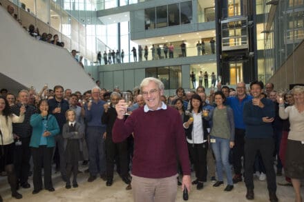 Richard Henderson holding a champagne glass aloft, stood in front of a large gathering of LMB celebrators