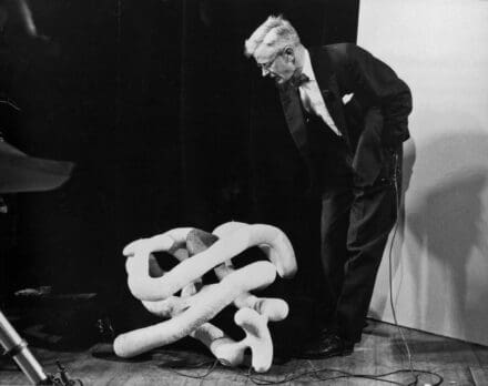 John Kendrew, stood leaning over a sausage model of myoglobin
