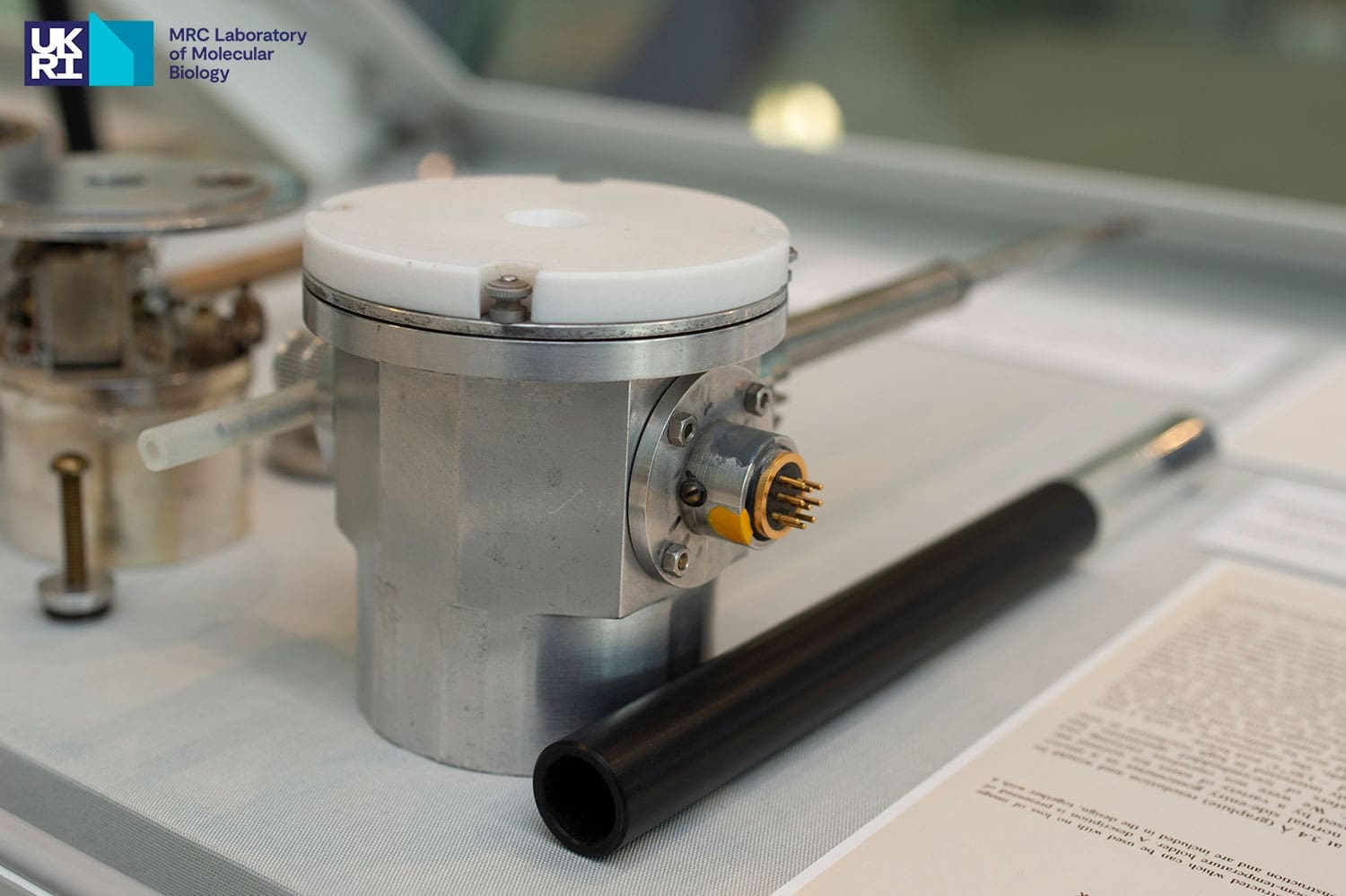 Silver-coloured cylindrical scientific instrument with a black tubular instrument placed next to it in a display case