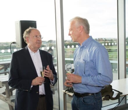 Andrew McKenzie speaking to Greg Winter, both hold champagne glasses