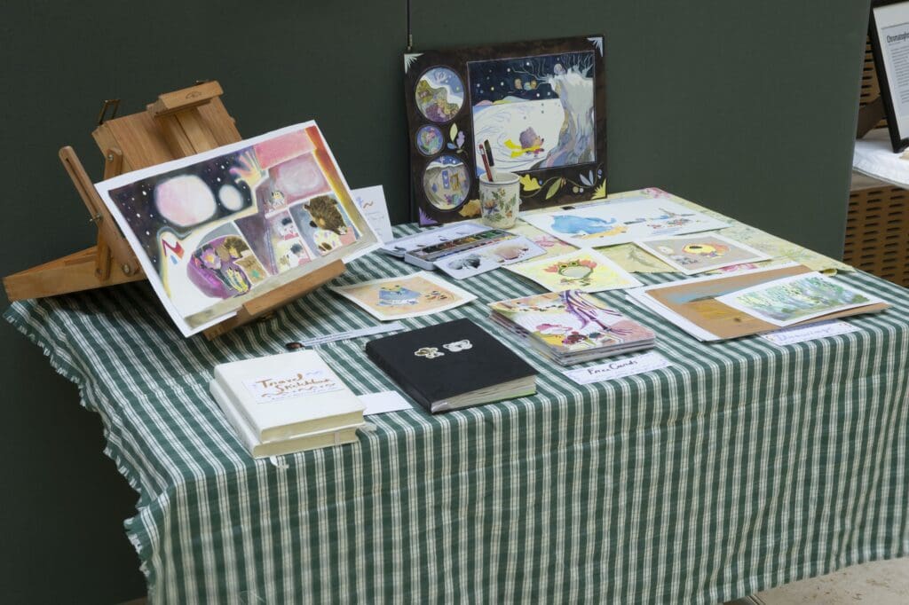 Table with green and white tablecloth diplaying illustration boards, pages, and books.