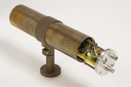 Brass metal tube on a stand, with one open end showing circuits and wires encased within