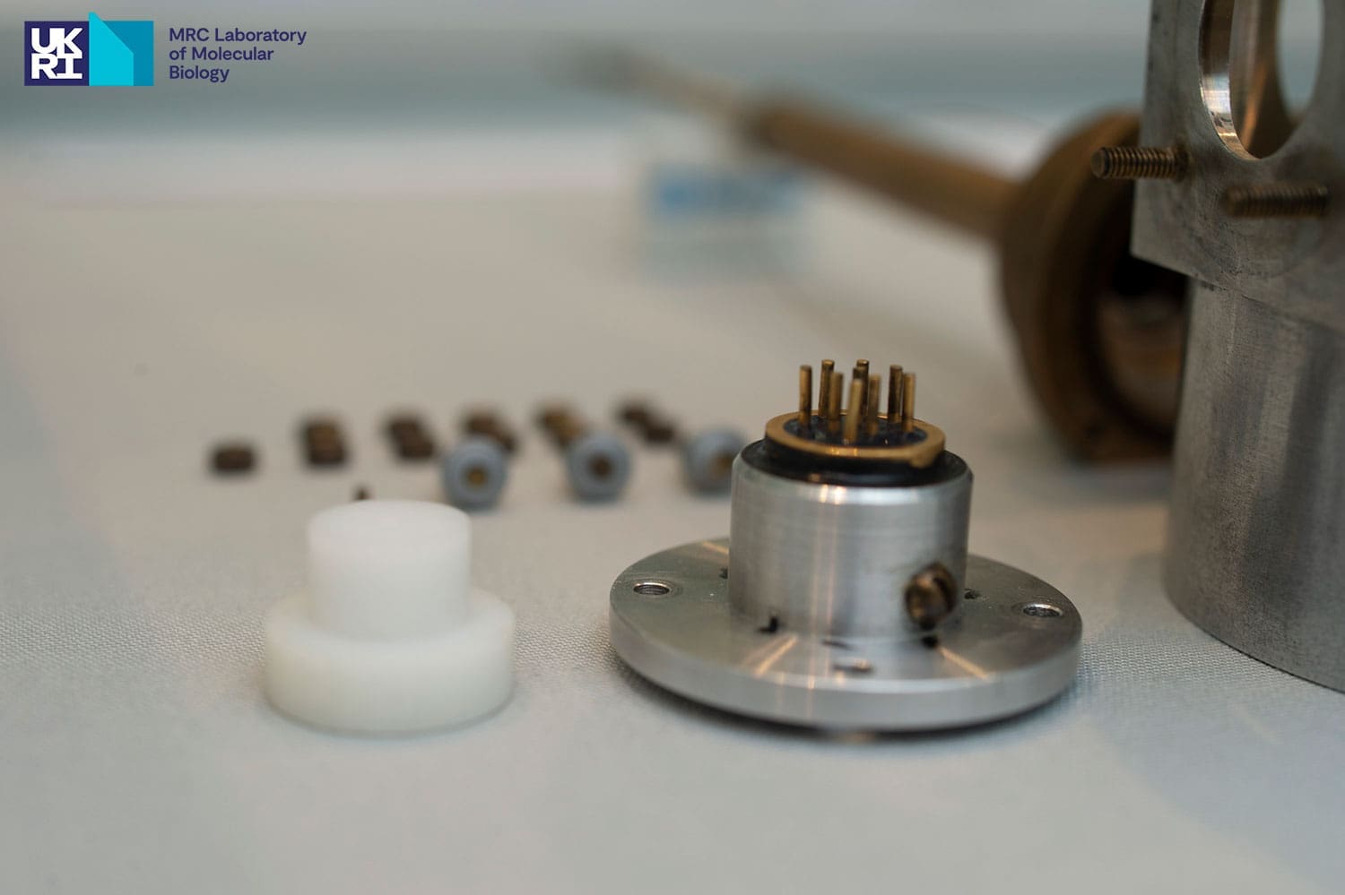 Two small pieces of scientific equipment in the foreground with metal nuts and fixtures out of focus in the background