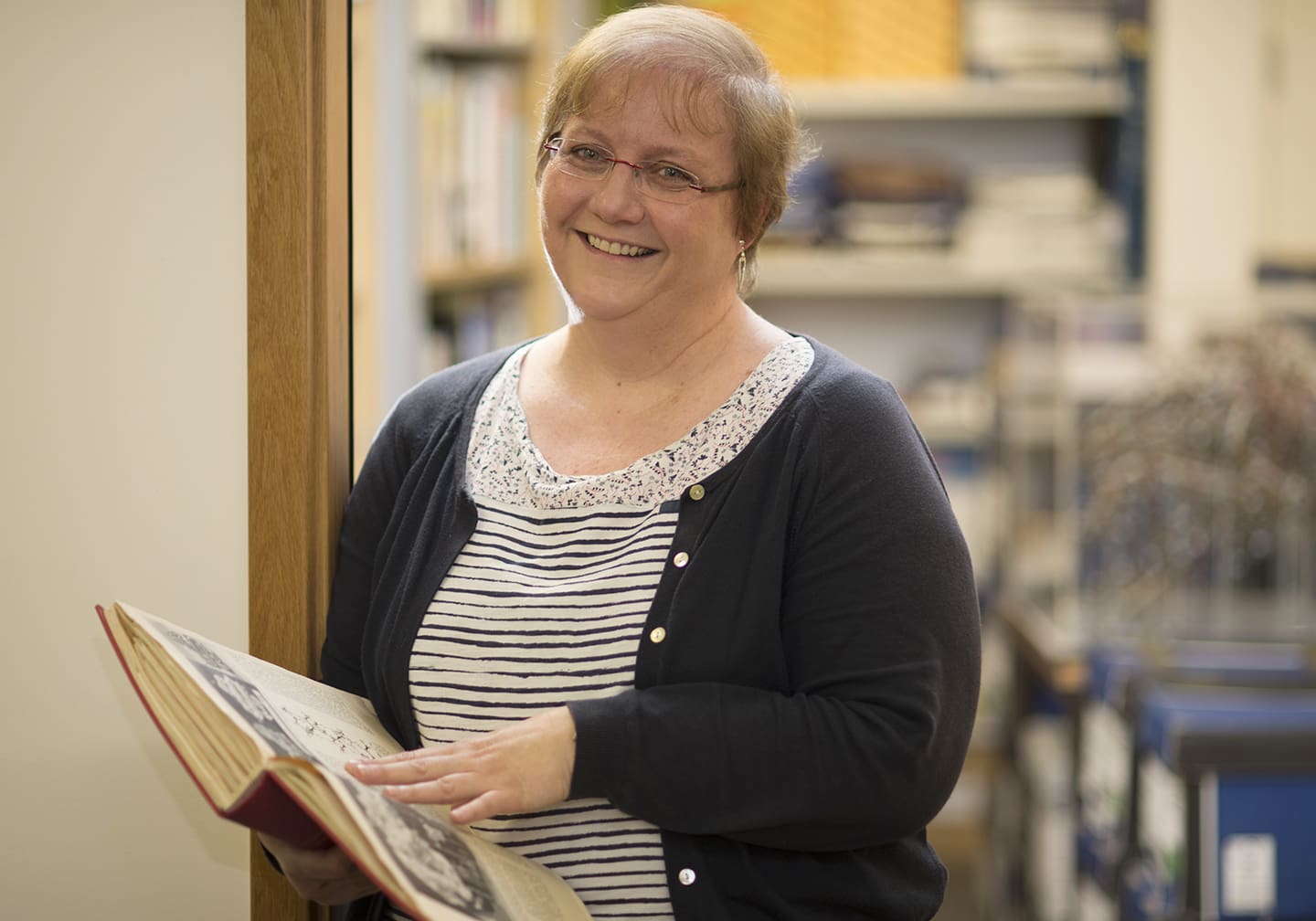 Annette Faux, smiling and holding an open book
