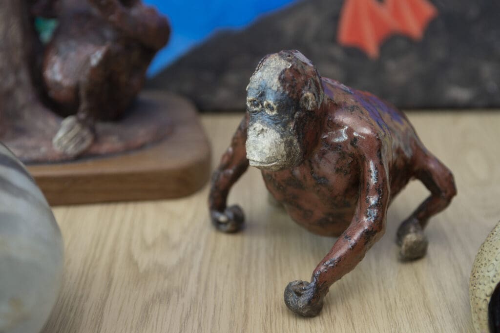 Image of a small statuette model of an orangutang placed on a table. Other models are partially visible in the background out of focus.
