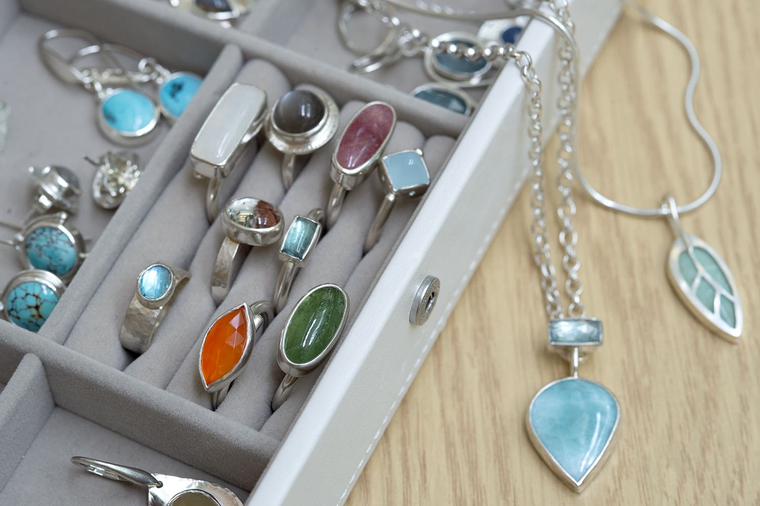 Close up of a jewllery box with visible hand-made jewellery including rings and necklaces with inset gemstones. 