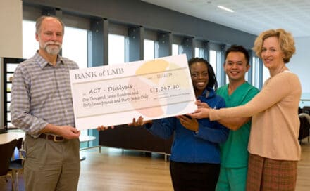 Four people hold a large novelty check for £1,747.30 to ACT - Dialysis in a modern room.