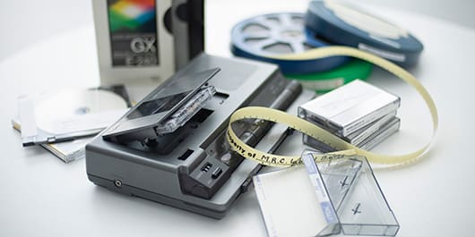 VHS tapes, CDs, cassettes, tape recorder, and film reels displayed together.