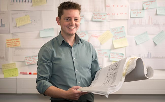 Man in front of a white board holding building plans.
