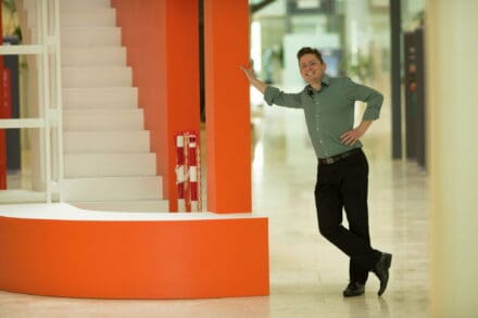 Stephen Holmes leaning against an orange wall in the LMB atrium